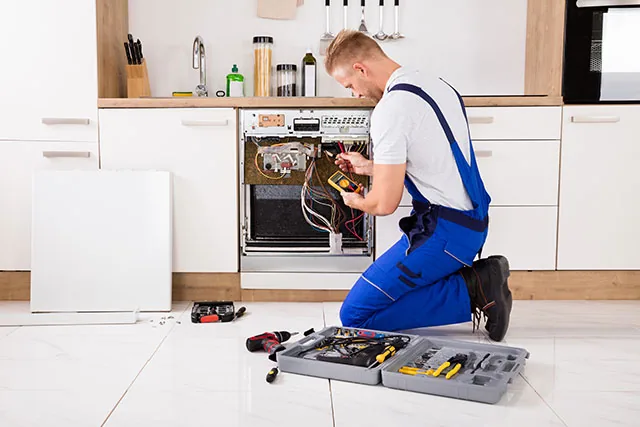 Technician testing electrical components in a kitchen range